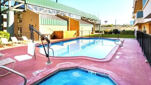 A swimming pool with a red deck, a covered area with a green roof, and a building with a beige facade in the background.