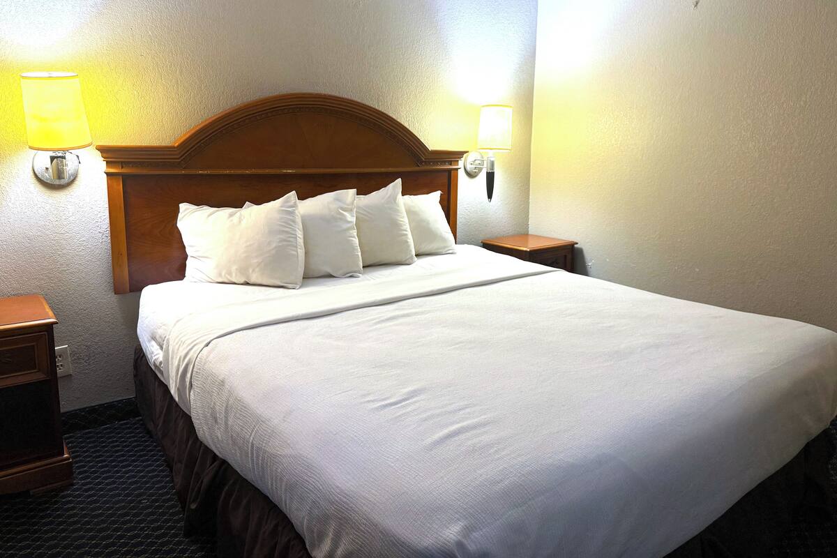 Una habitación de hotel con una cama grande, dos mesitas de noche y dos lámparas de pared.