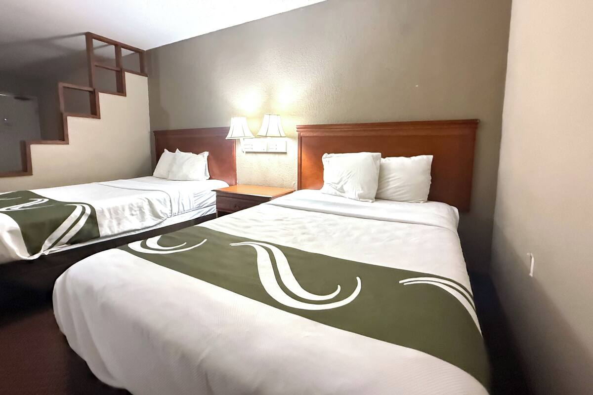 Dos camas individuales con cabeceros de madera, una mesita de noche con lámpara y una lámpara de pared.