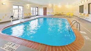 Une piscine intérieure avec des chaises jaunes, un panneau indiquant qu’il est interdit de plonger et un autre panneau similaire placé au bord de la piscine.