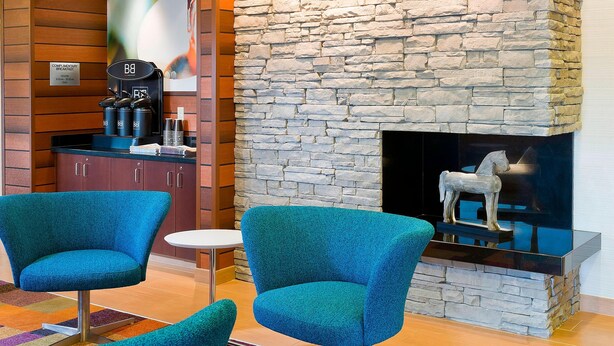 Un hall d’entrée avec une cheminée en pierre, deux fauteuils turquoise, un coin café et une petite table.