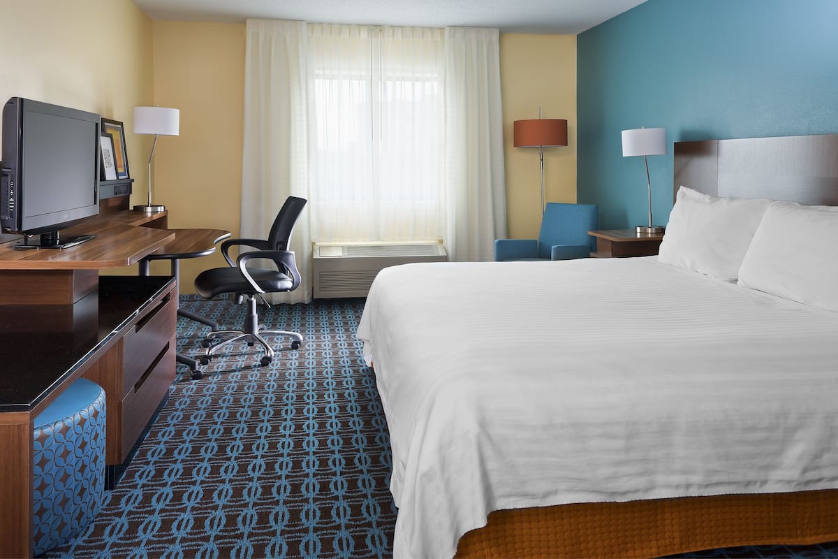 A hotel room with a bed, desk, chair, television, and lamps.