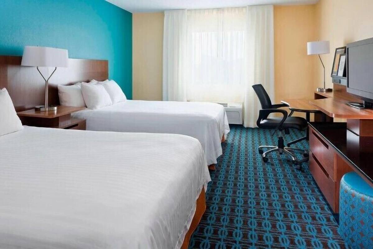 A hotel room with two beds, a desk, a chair, a television, and a window with curtains.