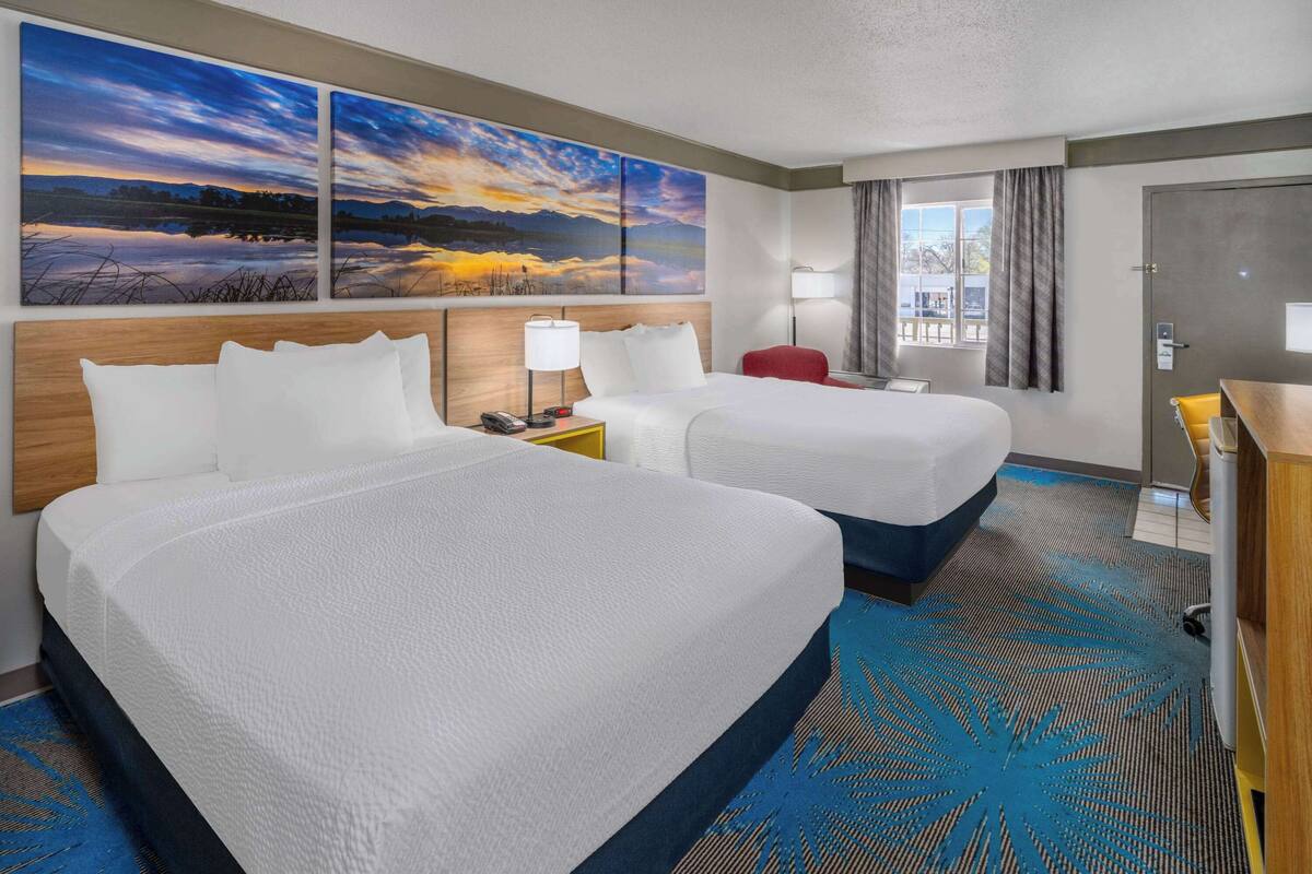 A hotel room with two beds, a desk, a chair, and a large window with curtains.