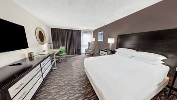 Habitación de hotel con una cama grande, un escritorio con silla, televisión y ventana con cortinas.