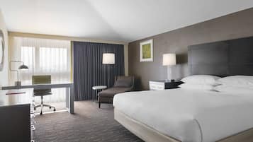 A hotel room with a bed, a desk, a chair, a nightstand, and a lamp.