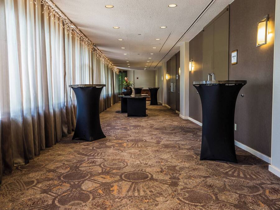 A hotel corridor with a patterned carpet, black podiums, and a row of curtains on one side.