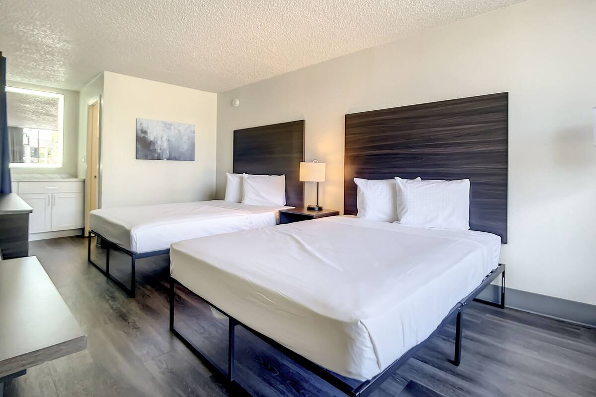A hotel room with two beds, a desk, a window, and a painting on the wall.