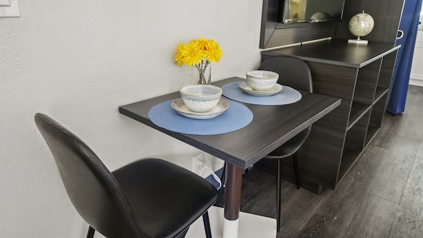 A dining table with two bowls and a vase of yellow flowers, a flat-screen TV, and a globe on a dark wooden shelf. - Stayable St. Augustine (St. Augustine)