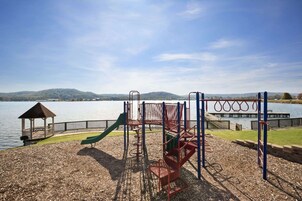 Un parque infantil con tobogán, estructuras para escalar y un pabellón junto a un lago.