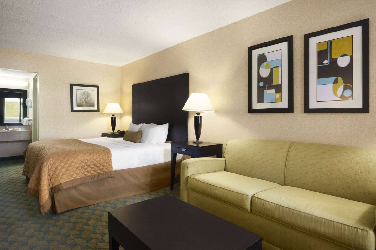Une chambre d’hôtel comprenant un lit, deux tables de chevet, un canapé et deux lampes fixées au mur.
