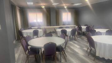 Un salón de conferencias con varias mesas redondas y sillas, ventanas amplias con cortinas, y piso de madera.