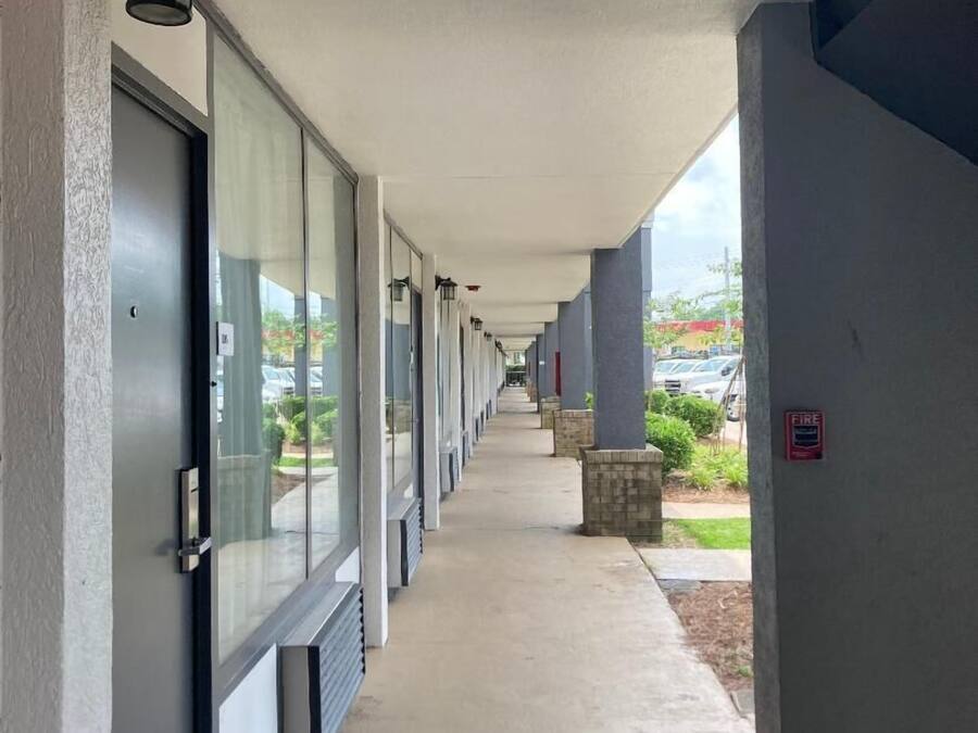 A covered corridor with doors, windows, and a fire alarm on the right wall.