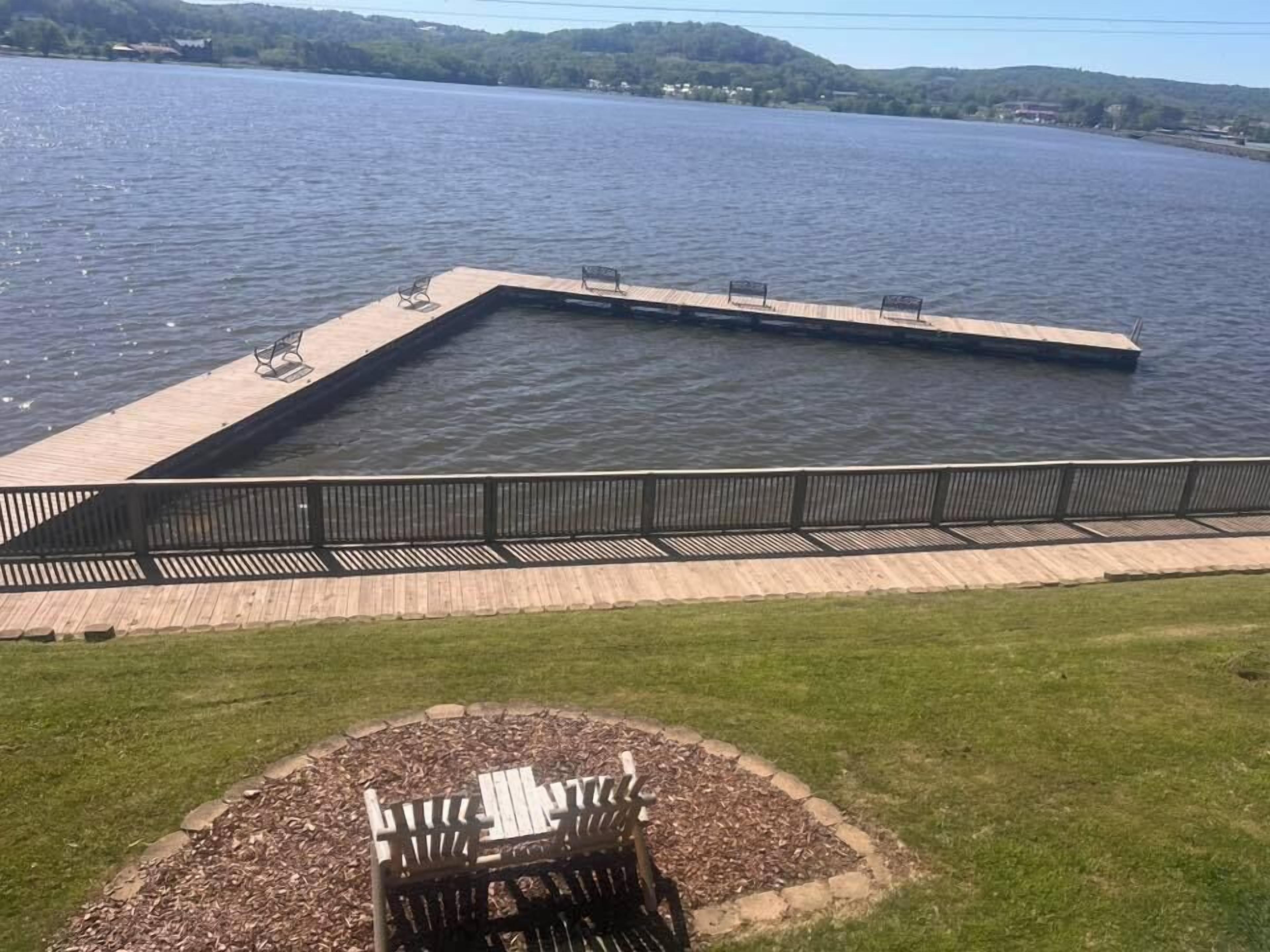 Un muelle que se adentra en un lago, con una zona de césped y un banco al frente.