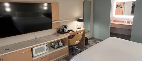Habitación de hotel con cama, escritorio con computadora, televisor, microondas y un espejo grande.
