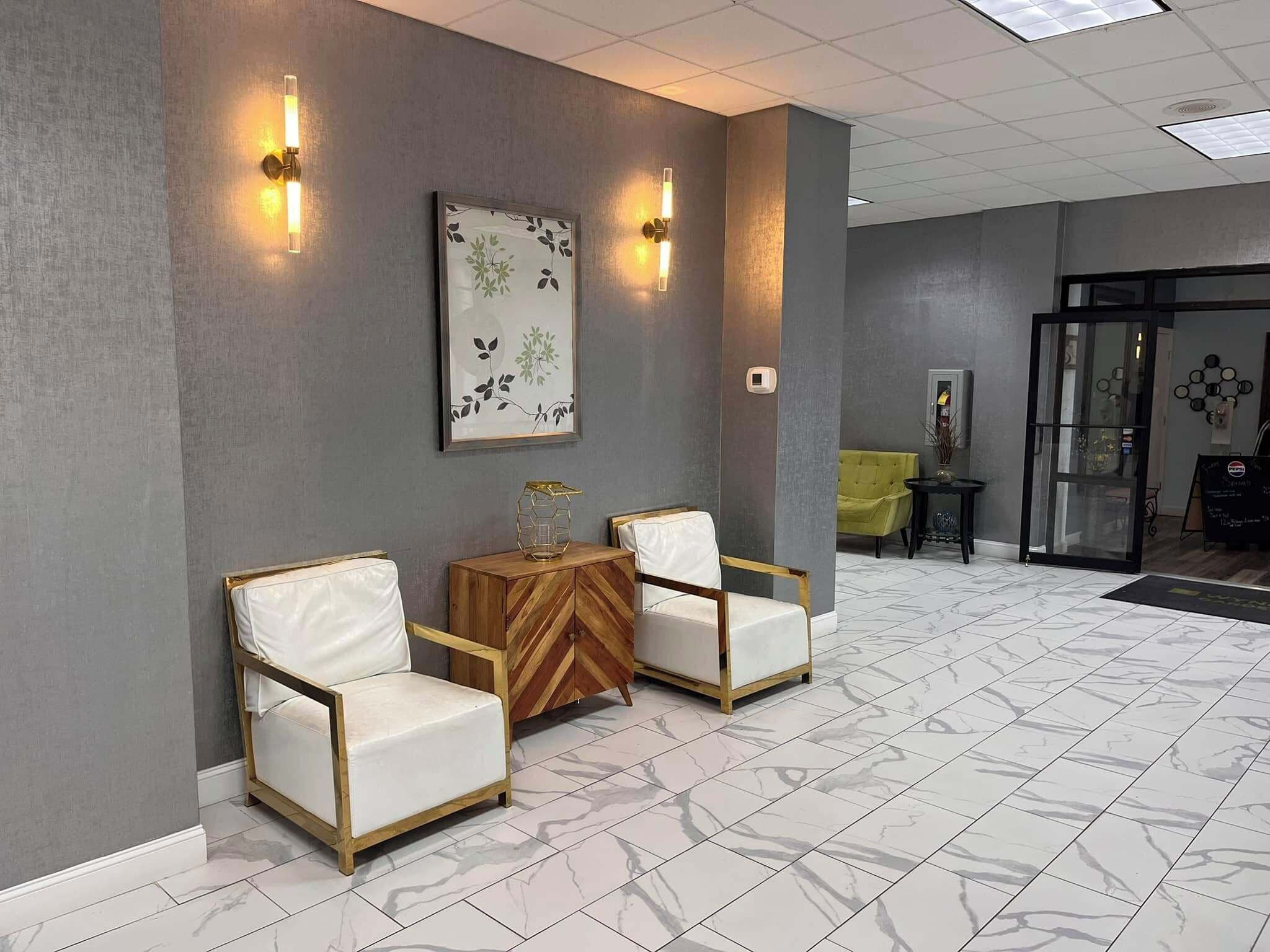 A reception area with two white leather chairs, a wooden side table, and a framed floral artwork on the wall.