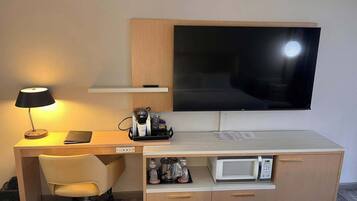 Une chambre d’hôtel équipée d’un bureau en bois, d’une télévision, d’un four à micro-ondes, d’une chaise et d’une table de chevet.