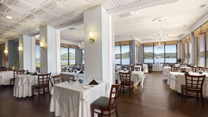 A spacious dining area with multiple tables and chairs, large windows with a view of a lake, and a high ceiling with decorative molding. - Wyndham Garden Lake Guntersville (Guntersville)