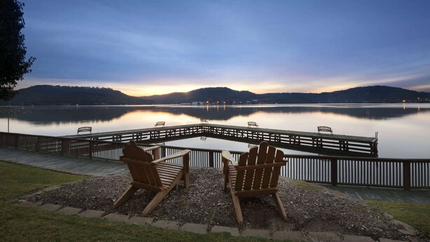 A lakeside deck with Adirondack chairs and a wooden dock extending into the water. - Wyndham Garden Lake Guntersville (Guntersville)