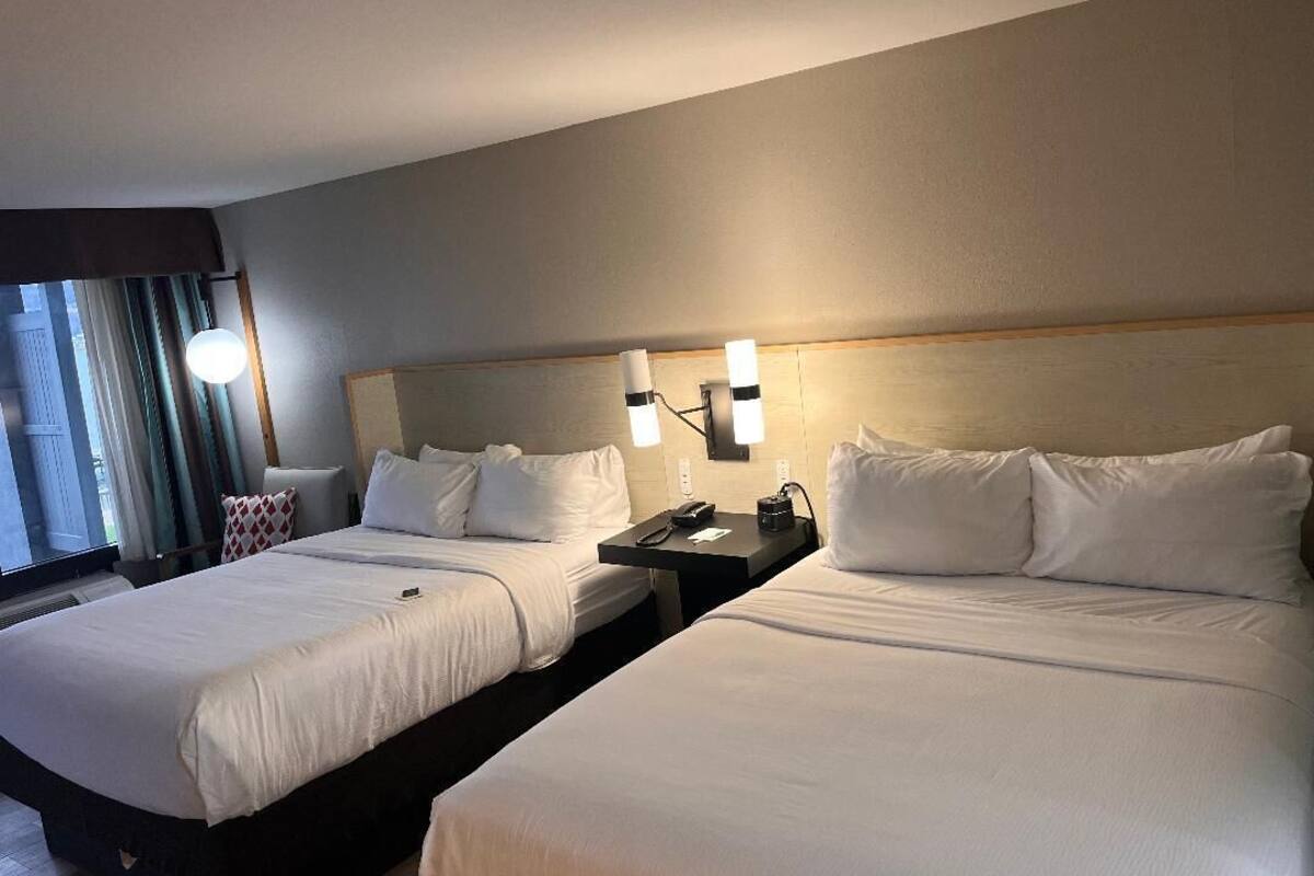 Une chambre d’hôtel avec deux lits, une table de chevet avec un téléphone et une fenêtre avec des rideaux.
