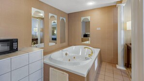 A modern bathroom with a large bathtub, a shower, and a microwave on the countertop.