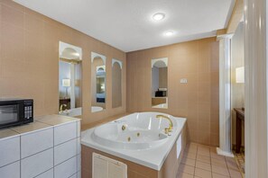 A modern bathroom with a large bathtub, a shower, and a microwave on the countertop.