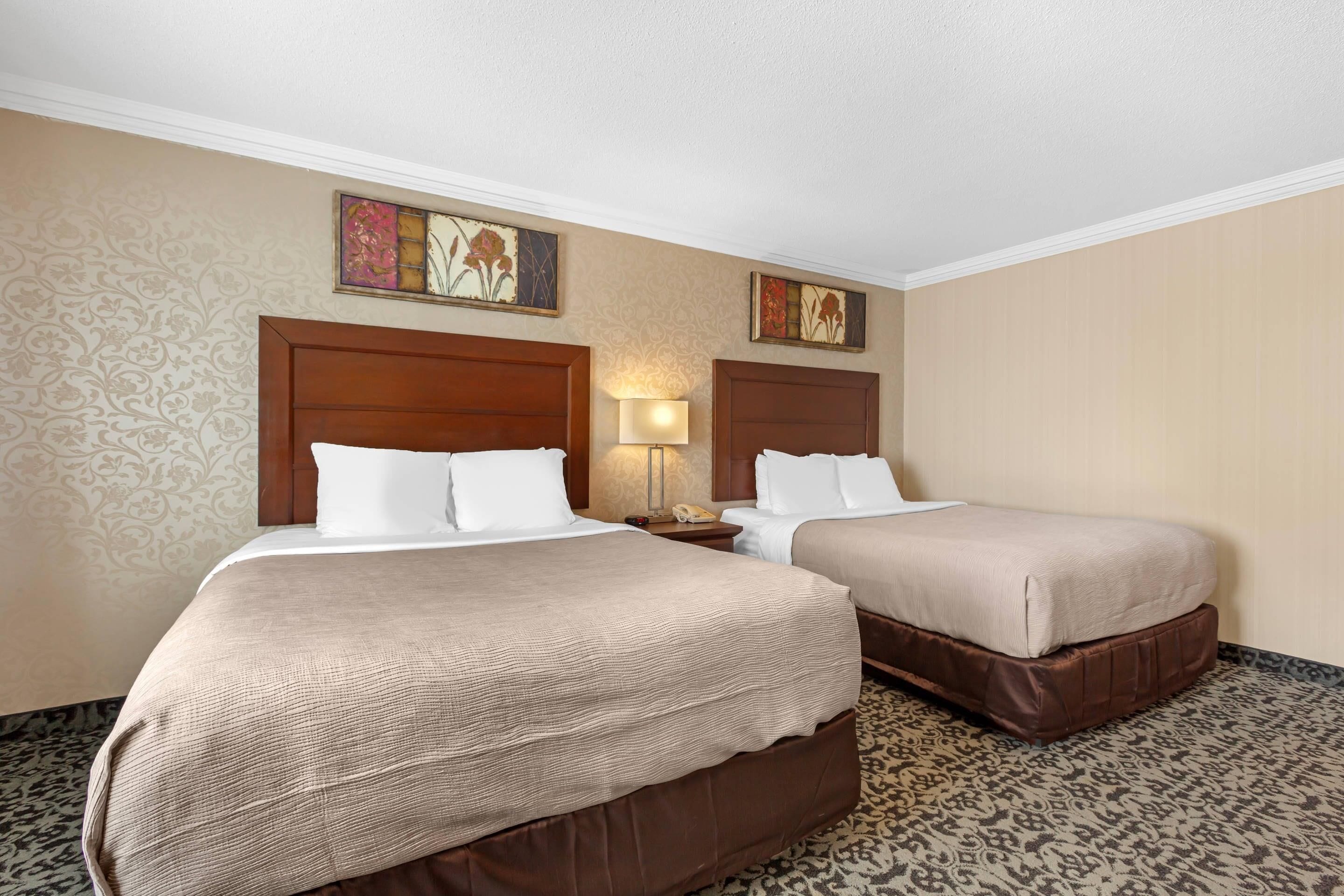 A hotel room with two beds, a nightstand, a lamp, and two wall-mounted paintings.