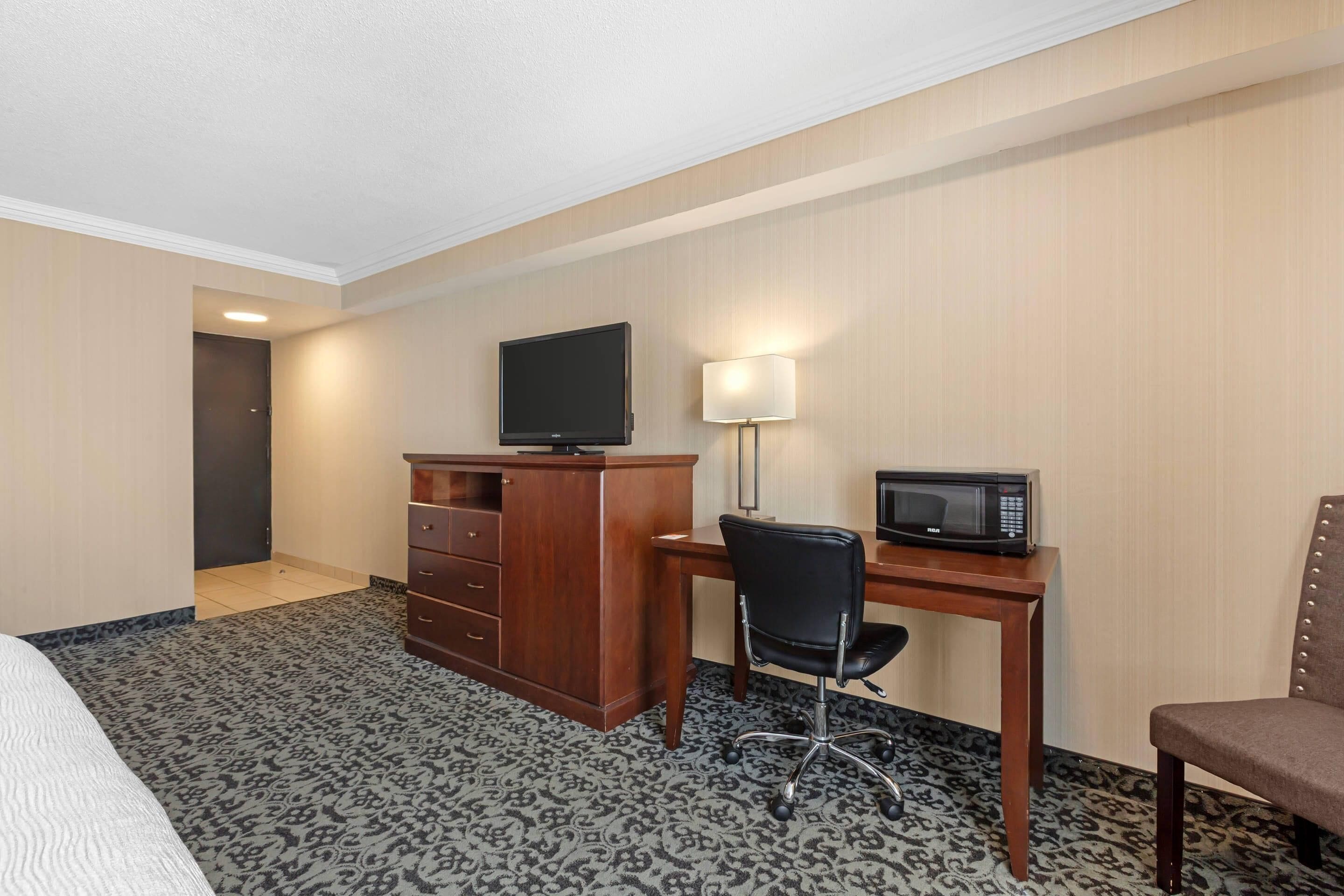 Habitación de hotel con cama, escritorio con computadora y televisor, microondas y una silla.