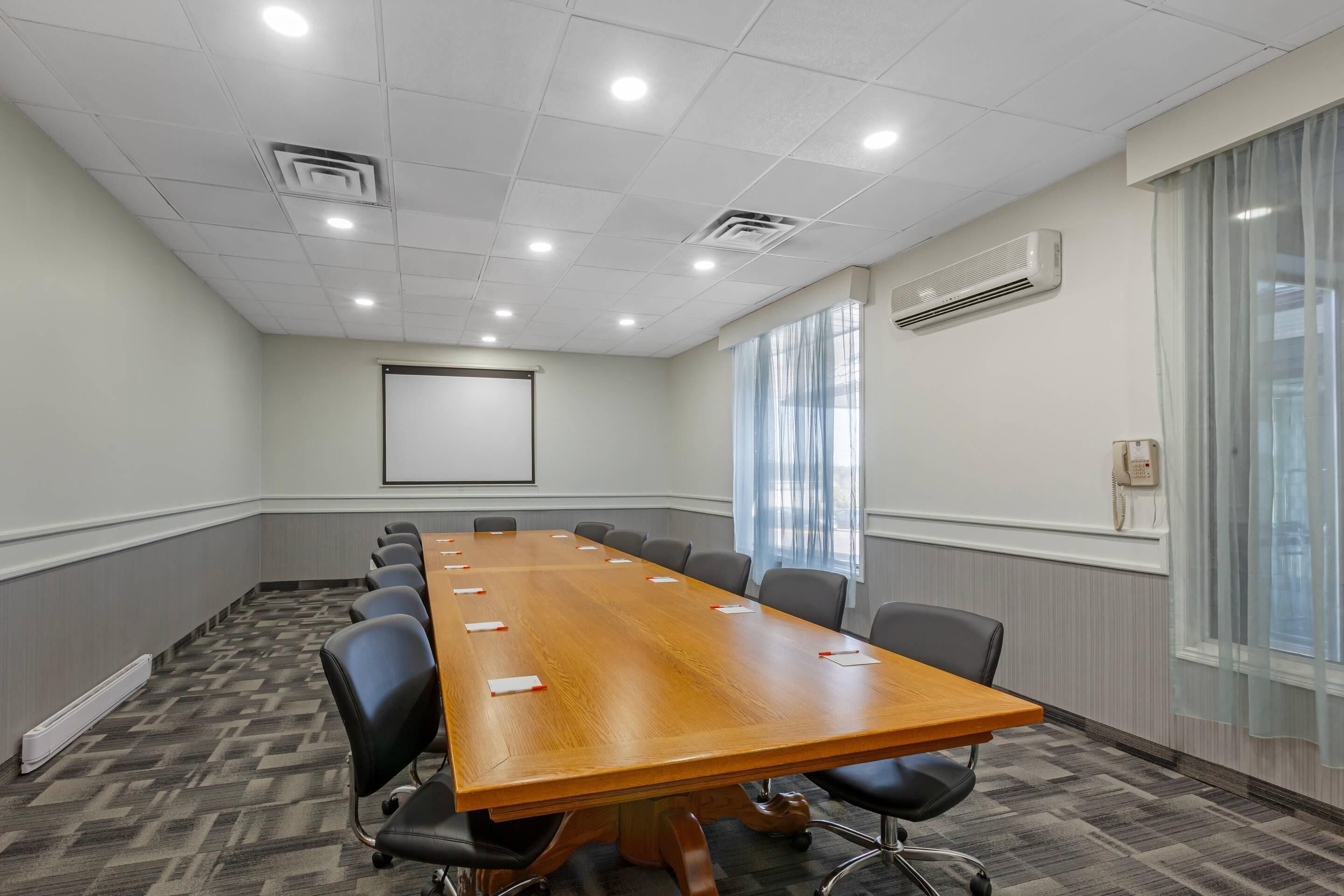A conference room with a long table, chairs, a projector screen, and windows with curtains.