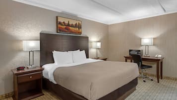 Una habitación de hotel con una cama grande, dos mesitas de noche con lámparas, un escritorio con silla y un cuadro sobre la cama.