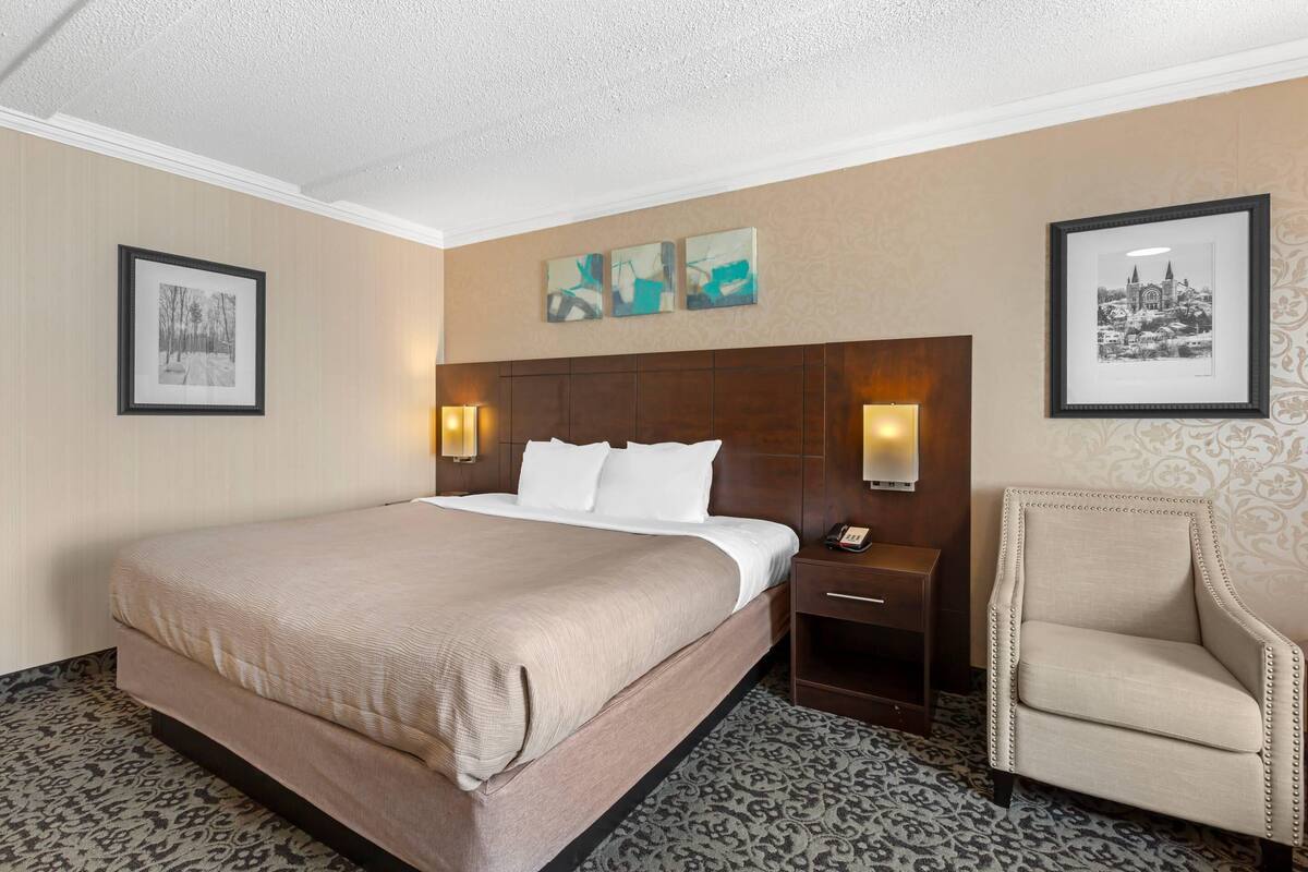 Una habitación de hotel con una cama grande, dos mesitas de noche con lámparas, una silla y cuadros en las paredes.