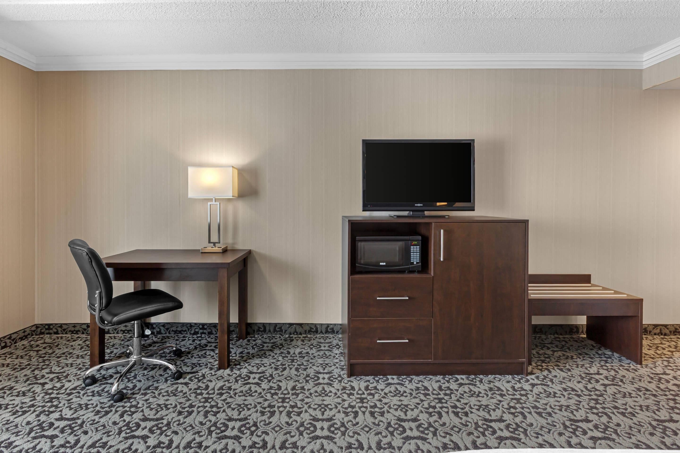 Ein Hotelzimmer mit Schreibtisch, Fernseher, Mikrowelle, Stuhl und einer Bank.
