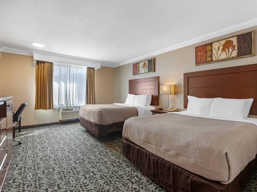 A hotel room with two beds, a desk, and a chair.