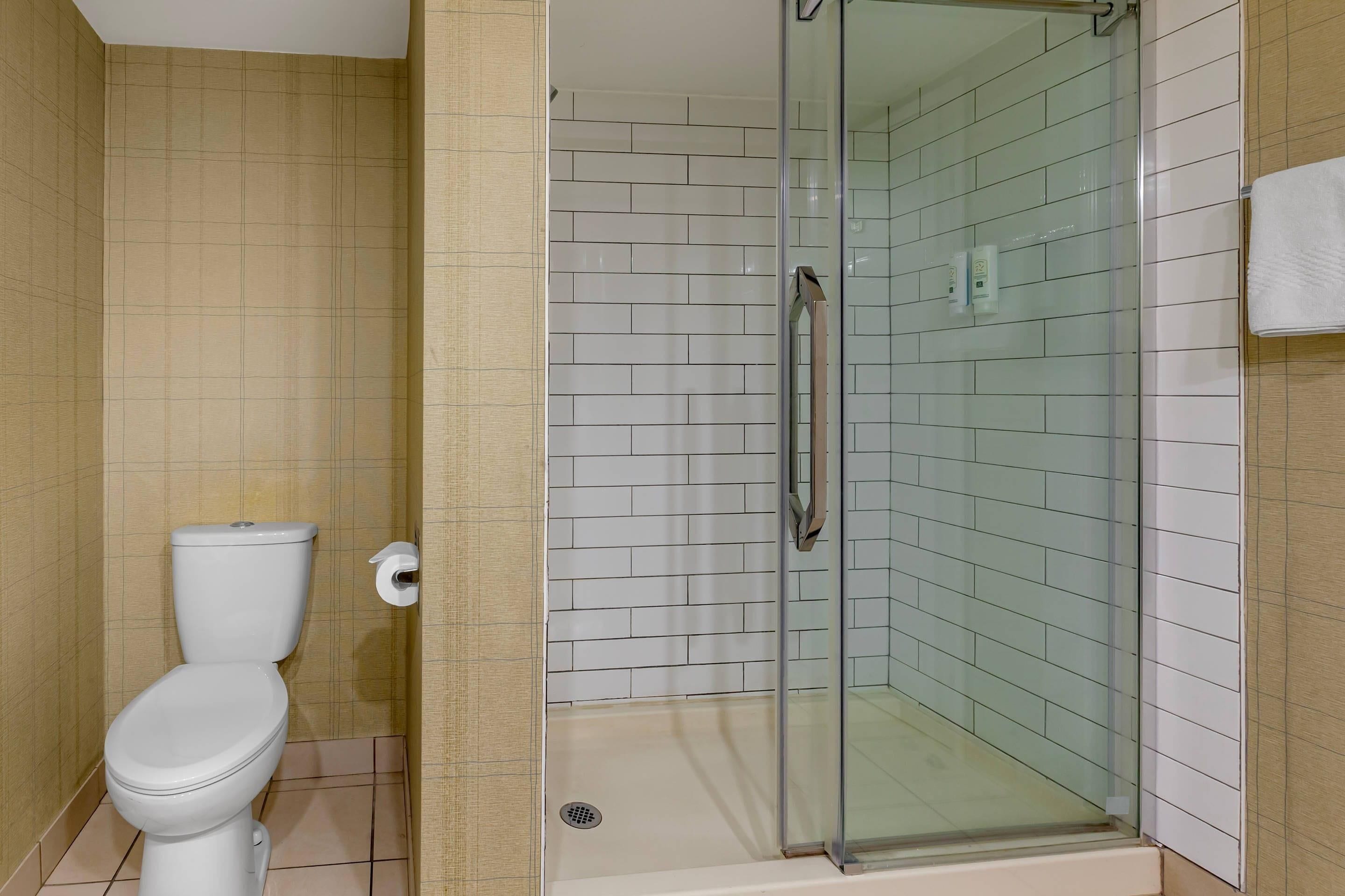 Een badkamer met toilet, een douchecabine van glas en betegelde wanden.