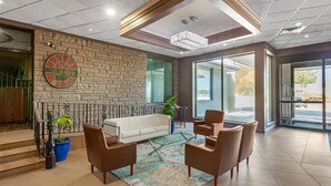 A modern lobby with a brick wall, a white sofa, brown chairs, a glass coffee table, and a chandelier. - Quality Inn & Conference Centre (Midland)