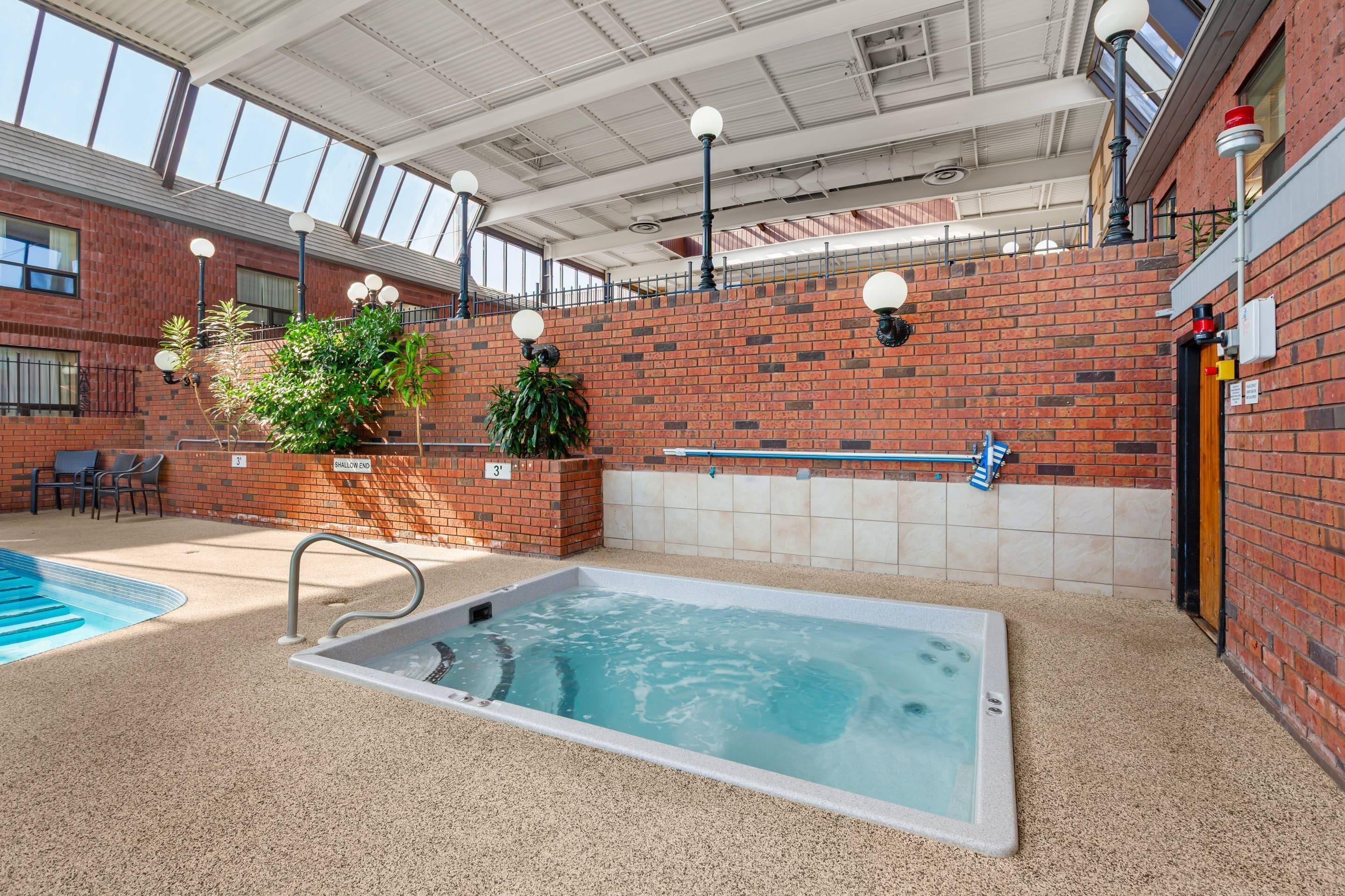 Una piscina interior con hidromasaje, rodeada de paredes de ladrillo y plantas en macetas.