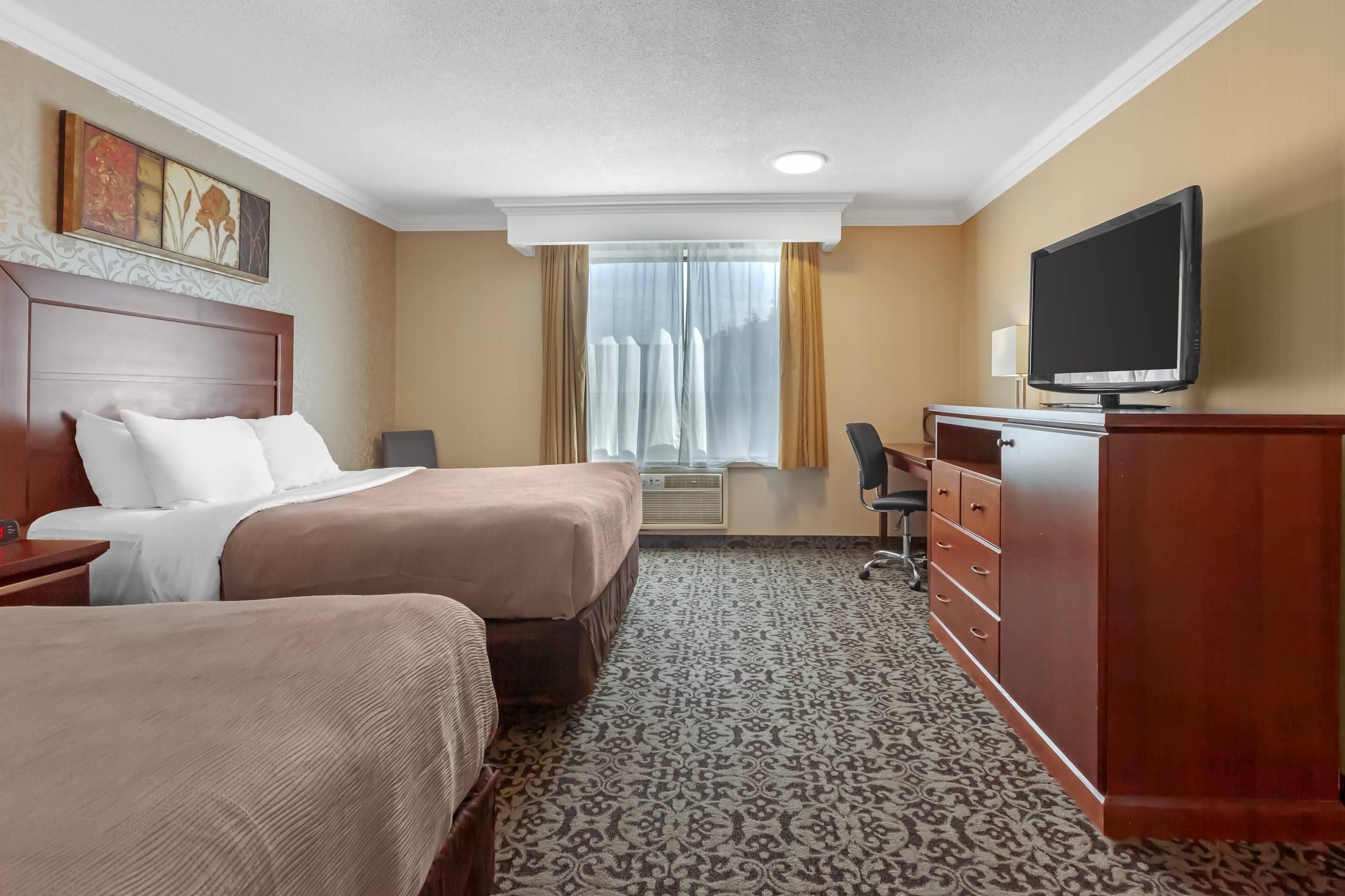 Habitación de hotel con dos camas, televisión, escritorio y cómoda.
