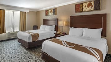 A hotel room with two beds, a desk, a chair, a lamp, and artwork on the walls.