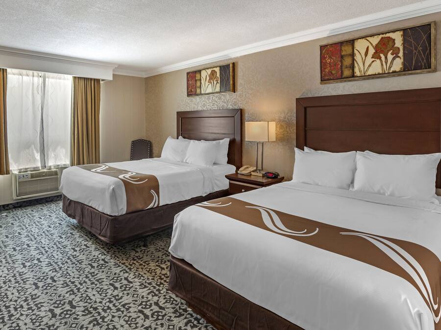 A hotel room with two beds, a desk, a chair, a lamp, and artwork on the walls.
