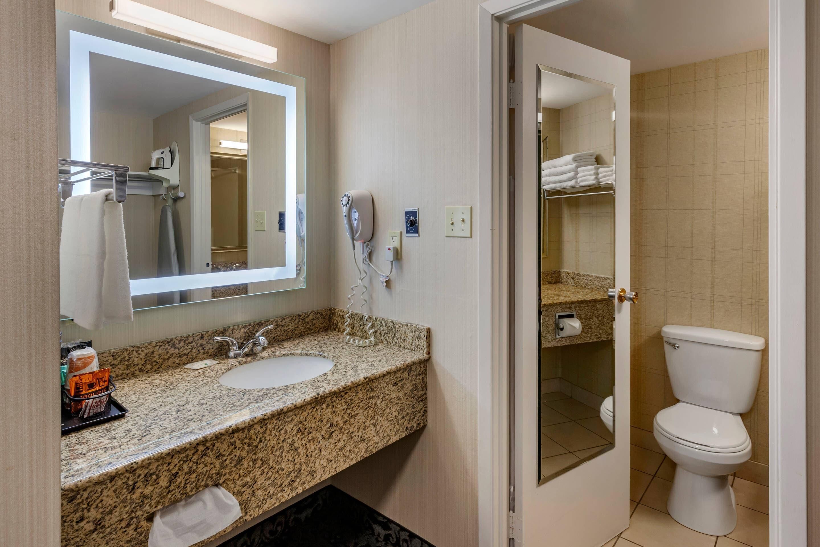 A bathroom with a granite countertop sink, a mirror, a hairdryer, and a toilet.