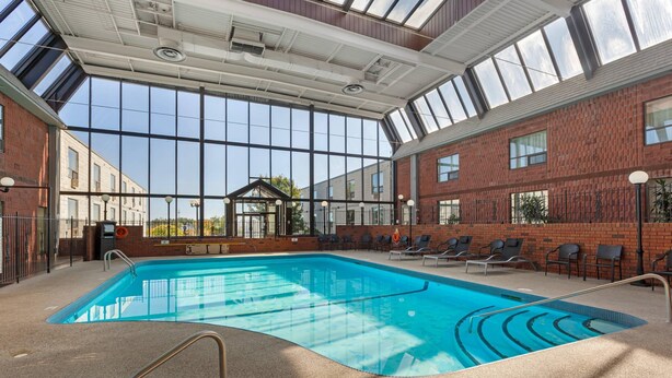 An indoor swimming pool with clear glass walls, a brick wall, and a sunroof. - Quality Inn & Conference Centre (Midland)