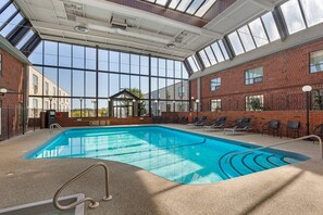 Una piscina interior con paredes de vidrio transparente, pared de ladrillo y tragaluz.