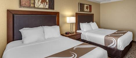A hotel room with two beds, a nightstand, a lamp, and artwork on the walls.