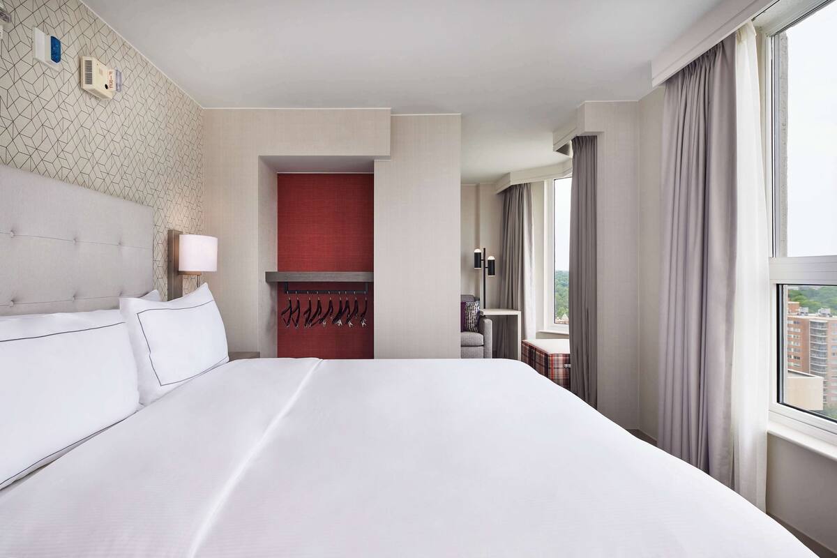 Ein Hotelzimmer mit einem großen Bett, einer roten Akzentwand, einer Sitzecke mit Tisch und einem Fenster mit Vorhängen.