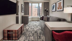 Une chambre d’hôtel avec une grande fenêtre, un téléviseur à écran plat, un canapé, une petite table et un fauteuil rouge.