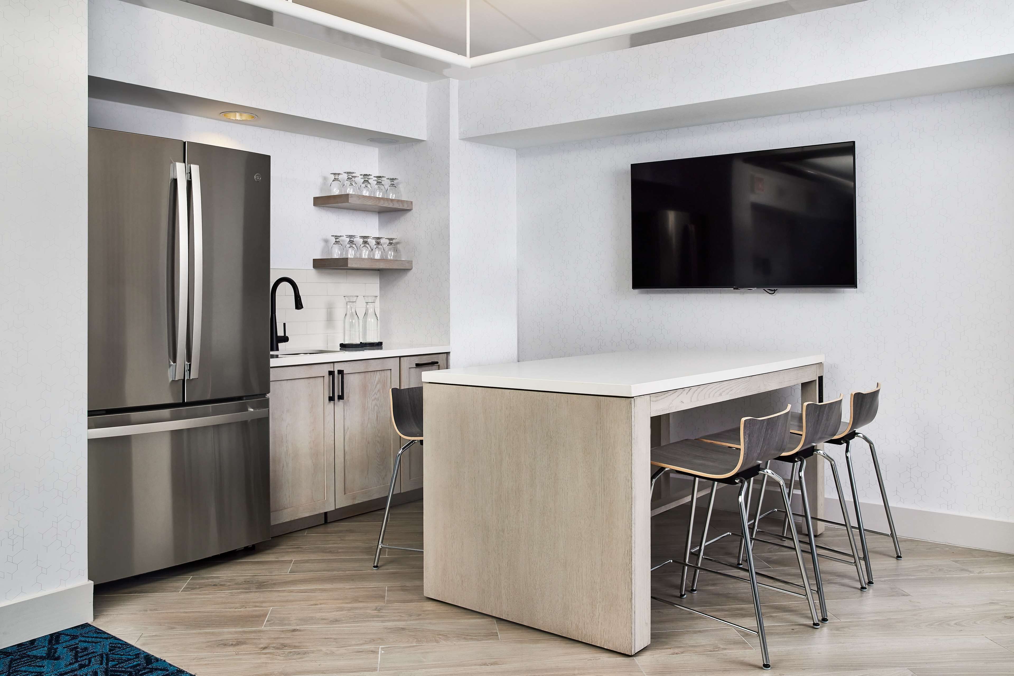 A modern kitchen with a built-in refrigerator, a flat-screen TV mounted on the wall, and a bar area with stools.
