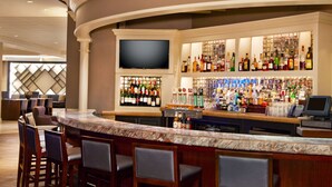 Un espace bar doté d’un comptoir en marbre, de plusieurs tabourets de bar, d’un téléviseur à écran plat et d’une étagère bien garnie de bouteilles d’alcool.