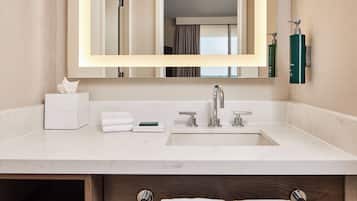 Une salle de bain moderne avec un grand miroir, un plan de toilette en marbre blanc et un lavabo intégré.