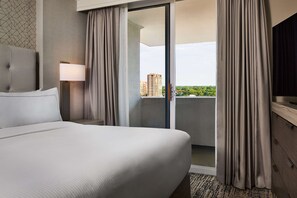 Une chambre d’hôtel avec un lit, une table de chevet avec une lampe, une porte-fenêtre coulissante donnant sur un balcon et un téléviseur posé sur une commode en bois.