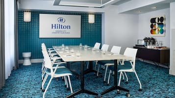 Una sala de conferències amb una taula llarga, cadires blanques i una catifa blava. Un gran pantalla mostra el logotip i el nom de Hilton.